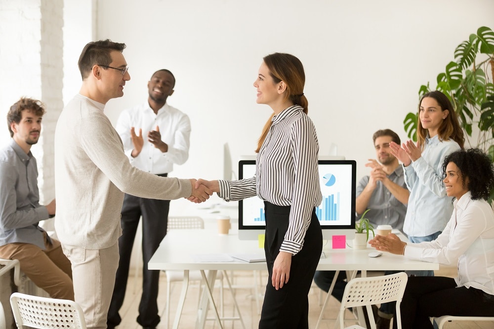 A room applauds as two people shake hands