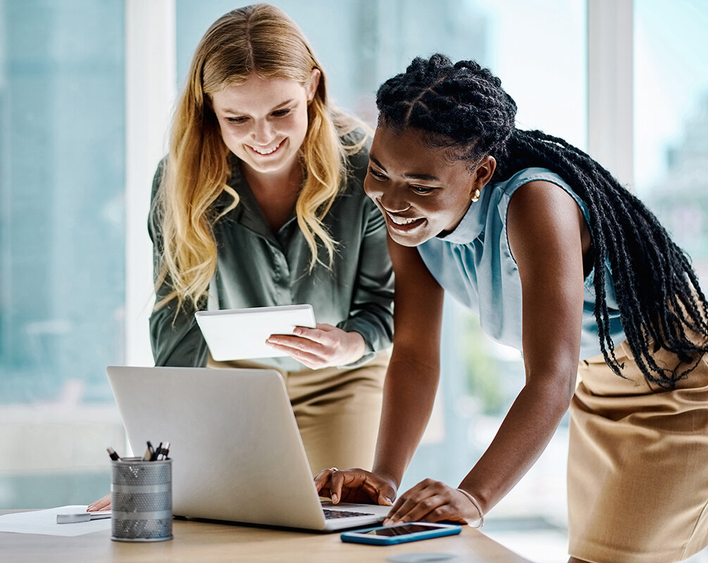 Two diverse businesswomen working together on a digital tablet and laptop in an office